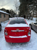 Red 2015 Chevrolet Sonic LTZ parked in snowy conditions, showcasing clear title and excellent condition.