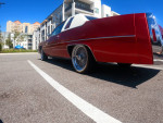 1997 Cadillac DeVille in candy apple red with chrome wire wheels, parked in a sunny residential area.