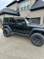 Black Jeep Wrangler Unlimited 4 Door SUV parked, featuring heavy duty bumper and off-road tires.