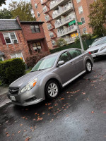2010 Subaru Legacy in silver parked on a rainy street, showcasing its AWD and spacious design.