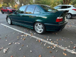 1997 BMW M3 E36 in green with alloy wheels parked among autumn leaves, showcasing its sporty design.
