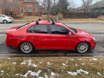 Red Volkswagen Jetta GLI parked on a snowy street, showcasing its sporty design and roof rack features.
