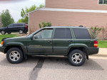 1997 Jeep Grand Cherokee with 150,000 miles, showing faded paint and functional front seats, parked outside