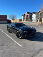 2010 Chevrolet Camaro RS in black, parked with trees and buildings in the background, showcasing its sporty design.