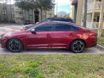 2023 Kia K5 GT-LINE in passion sport red parked on a grassy area, showcasing its sleek design and sporty wheels.