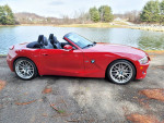 BMW Z4 M Roadster in red parked near a serene lake, showcasing low mileage and excellent condition.