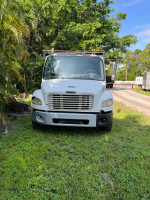 Front view of a 2004 Freightliner M2 mechanic special for parts, on a grassy area with trees.