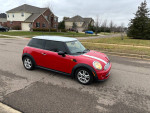 2013 Mini Cooper in red, showcasing its sleek design and compact size on a suburban street.