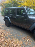 2023 Jeep Wrangler Sport 4WD parked on a scenic road surrounded by autumn foliage.