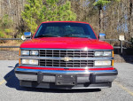 Front view of a red 1989 Chevrolet Silverado C1500 pickup truck with a clear sky and trees in the background.
