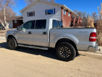 Side view of a 2004 Ford F150 XLT pickup truck in silver with custom wheels, parked outdoors.