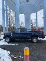 2019 F-250 Superduty truck parked near a water tower, featuring a bed liner and Boss plow mount.