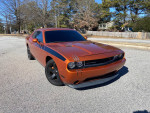 2011 Dodge Challenger in bright orange, customized with unique stripes, parked on a sunny street.
