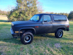 1987 GMC Jimmy Sierra Classic with fresh black paint and new tires parked in a green field