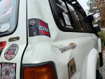 Side view of a Toyota Tacoma showcasing stickers and minor body damage, highlighting off-road modifications.