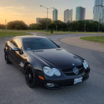 2008 Mercedes-Benz SL 550 in black parked with city skyline at sunset, showcasing sleek design and good condition.