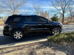 2016 GMC Acadia Denali FWD parked on the road, featuring chrome wheels and a sleek black exterior.