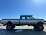 1995 Ford F350 Quad Cab 4WD side view with a monster lift and new tires against a clear blue sky