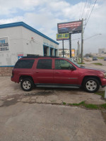 2003 Chevrolet TrailBlazer parked outside a repair shop with a sign promoting quick inspections.