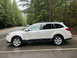 2011 Subaru Outback 2.5i AWD parked in a forested area, showcasing its sleek design and all-wheel drive capability.