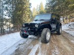2009 Jeep Wrangler Rubicon 4WD parked on snowy dirt road surrounded by trees, showcasing its rugged design.