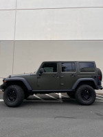 2015 Jeep Wrangler Rubicon in Tank Green, well-maintained with aftermarket accessories parked in a lot.