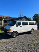 1997 Dodge 3500 15 passenger van in white, parked on gravel with a house in the background.