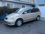2002 Honda Odyssey van with heated leather seats, parked outside a house, showcasing its well-used exterior.