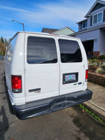 Rear view of a 2012 Ford E-250 van parked in a residential area, showcasing its storage cabinets and clean condition.