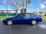 2006 Chevrolet Impala SS in blue, showing side profile, parked in a green area with trees.