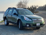 2013 Subaru Outback in green, parked by the water, showcasing its exterior and new tires