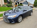 2015 Toyota Camry XLE in navy blue parked on a residential street with trees and houses in the background.