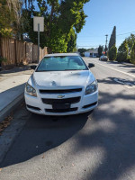 Front view of a 2012 Chevrolet Malibu LS parked on the street with some minor damage.