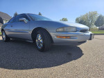 1997 Buick Riviera Supercharged coupe parked on a sunny day, showcasing its sleek design and chrome wheels.