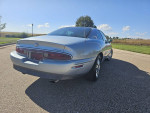 Rear view of a 1997 Buick Riviera Supercharged coupe parked outdoors, showcasing its chrome wheels and sleek design.