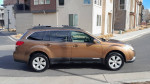 2012 Subaru Outback 2.5i AWD in brown parked on a residential street, showcasing its sporty design.