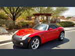 2006 Pontiac Solstice in red parked on a sunny street, showing its sleek design and convertible roof.