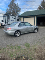 Well-maintained Subaru Impreza with body damage, parked in gravel, featuring new all-weather tires.