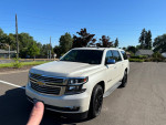 2015 Chevrolet Suburban LTZ in white with black wheels parked in a clear blue sky setting
