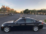 Side view of a black 2015 BMW 5 Series 528i parked in a lot with trees in the background.