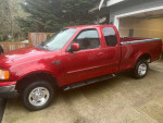 1999 Ford F-150 XLT 4WD in red, showcasing excellent condition and new tires, parked in a residential area.