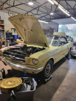 1965 Ford Mustang with the hood open in a garage, showcasing the engine and restoration work.