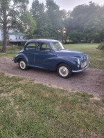 Classic 1963 Morris Minor parked on a gravel driveway, surrounded by grass and trees.