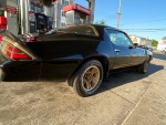 1980 Chevy Camaro Z28 parked by a gas station, showcasing its sleek black exterior and gold wheels.