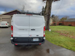 Rear view of a 2016 Ford Transit Cargo Van with 86,000 miles parked in a residential area.