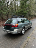 2001 Subaru Outback AWD parked on a forested road, showcasing its excellent condition and glossy paint.