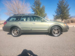 2005 Subaru Outback in green, showcasing its side profile and alloy wheels in a scenic outdoor setting.