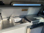 Interior view of the kitchen area in a 1999 Volkswagen EuroVan camper with sink and stove.