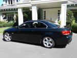 Sapphire black 2009 BMW 328i convertible parked in front of a house, showcasing low mileage and elegant design.