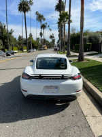 Rear view of a 2018 Porsche 718 Cayman parked on a sunny street with palm trees.